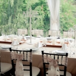 Clear tent with a blush, white and black wedding reception table decked out with candelabras and table settings and bow-tied black Chivari chairs